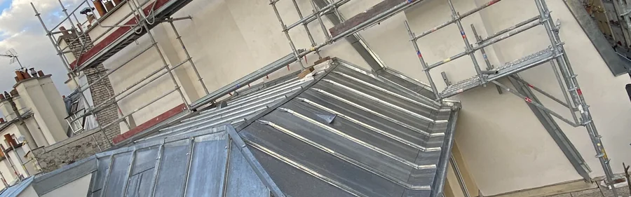 Couverture zinc neuve à noues et arêtiers sur un immeuble parisien, échafaudage en place et toits de Paris en arrière-plan