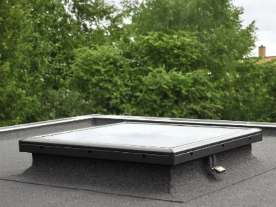 Fenêtre de toit VELUX pour toit plat à vitrage plan, posée sur sa costière raccordée à l'étanchéité