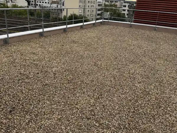 Toit terrasse sous gravillons d'un immeuble résidentiel parisien, garde-corps et barres d'immeubles en arrière-plan