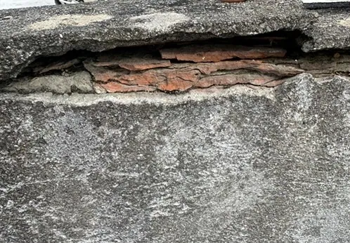 Tête de mur en couronnement d'un toit terrasse, enduit éclaté laissant apparaître les briques