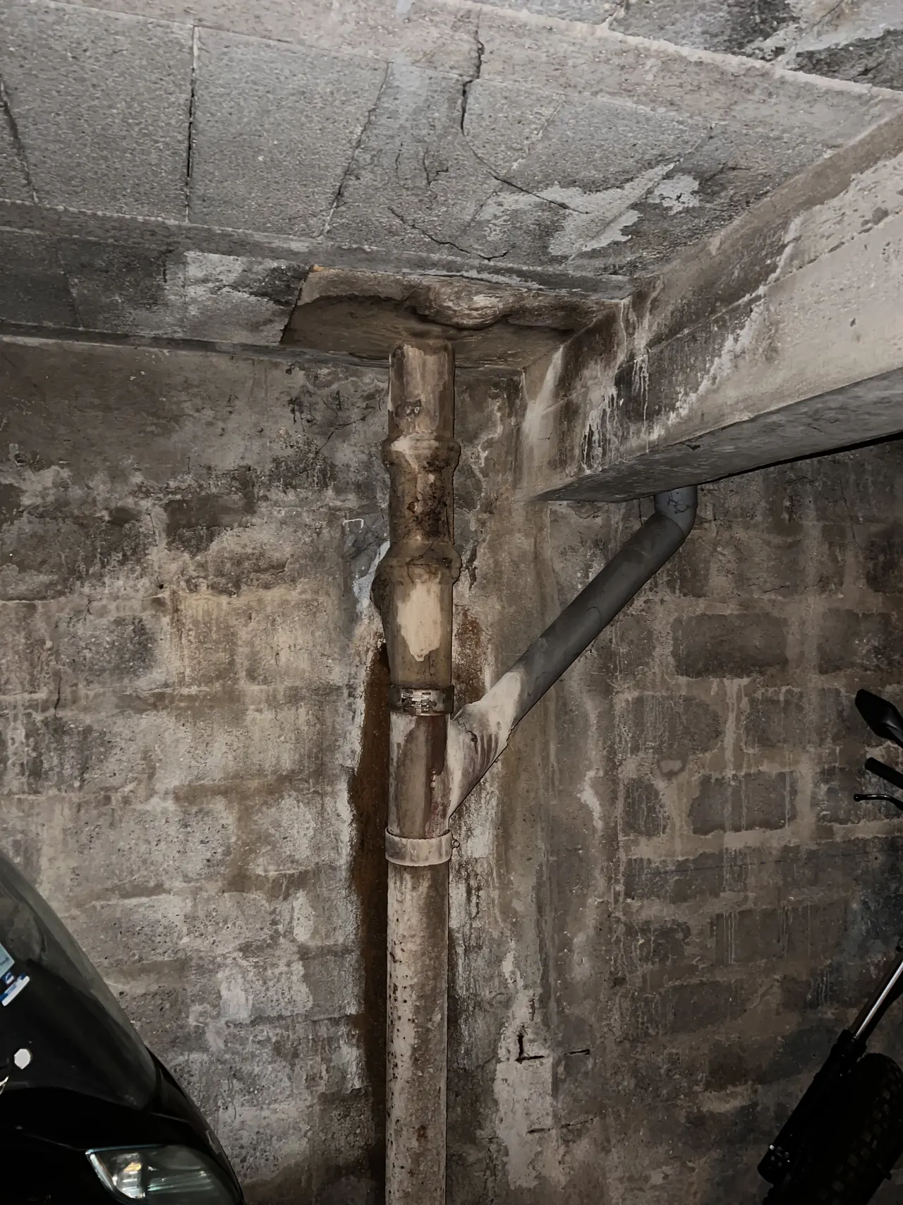 Descente d'eaux pluviales en fonte dans le sous-sol d'un immeuble parisien, traces blanches sur le mur et le plafond