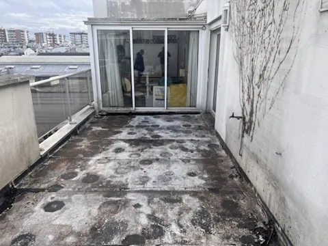 Terrasse d'appartement au revêtement ancien très encrassé, traces noires et blanches devant une baie vitrée